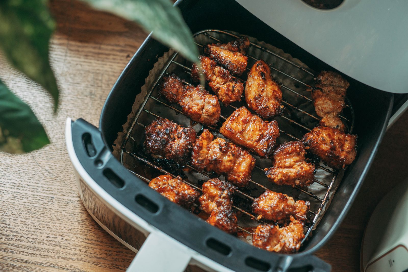 Cesta de air fryer aberta com pedaços de frango dourados e crocantes sobre uma mesa de madeira